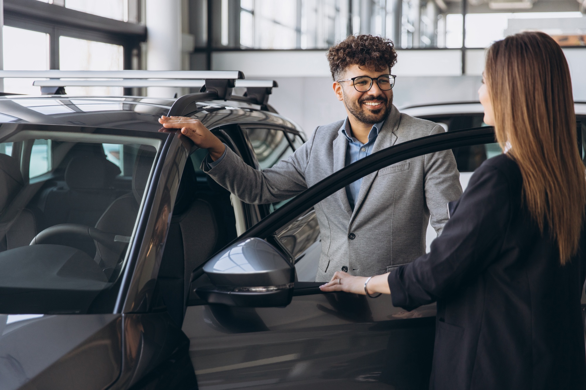 Car salesman showing new vehicle to customer in dealership