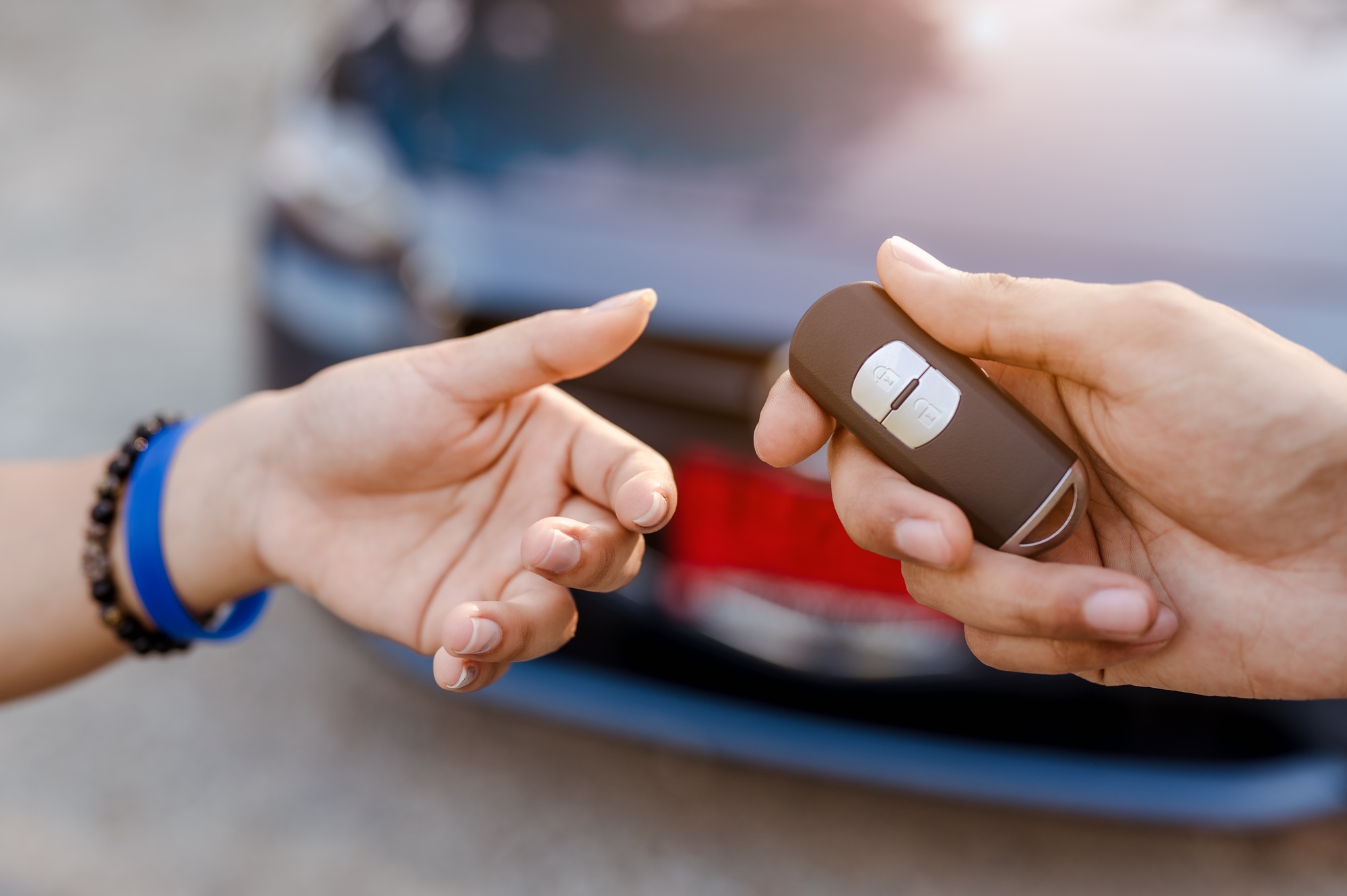 Close up woman holding new car systems key of blue hatchback car after buying from dealer at outdoor